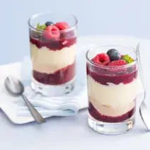 fotografia em tons de branco e vermelho tirada de dois copos transparentes com geleia de frutas vermelhas e leite MOÇA de colher com frutas vermelhas por cima e colheres ao lado.