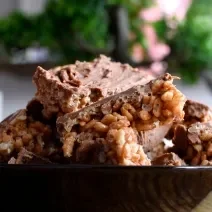 Fotografia de alguns docinhos com cobertura de Chocolate ao Leite GAROTO com crespinho de arroz dentro de um recipiente preto fundo.