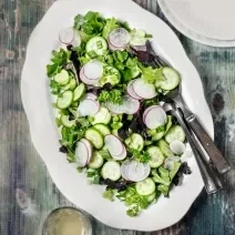 Fotografia vista de cima de um recipiente de vidro raso branco, com uma salada de acelga com cebolinha-verde com tempero, vinagre, azeite e limão.