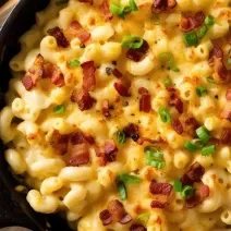 Fotografia vista de cima de macarrrão com queijo e bacon dentro de uma penela preta, sobre uma tábua de madeira.