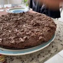 Fotografia de uma torta de chocolate com raspas de chocolate sobre um apoio branco com borda azul.