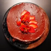 Fotografia em tons de marrom com um prato marrom ao centro. Em cima do prato existe uma receita de torta mousse de chocolate coberta com morangos e flores comestíveis.