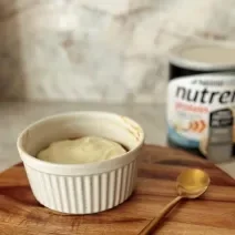 Foto da receita de cookie de airfryer feito com Nutren Protein, servido e um pote branco com uma cobertura branca por cima e a lata do produto ao fundo