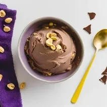 Fotografia em tons de branco com uma tigela ao centro. Dentro da tigela existe um sorvete de chocolate com pedaços de amendoim em cima.