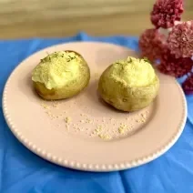 Fotografia em tons de azul e rosa com um prato rosa ao centro. Dentro do prato existe duas batatas recheadas com creme de ASCENDA e polvilhadas com queijo parmesão