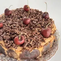 Fotografia em tons de branco com um bolo de Cuca de maçã verde ao centro enfeitada com cerejas