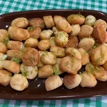 Foto aproximada da receita de pinholate de natal, bolinhas pequenas e crocantes, servidas todas em uma travessa marrom, cobertas com mel e raspas de limão