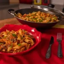 A fotografia mostra penne al dente coberto com molho de tomate caseiro, carne moída bem temperada, azeitonas e mostarda, finalizado com cebolinha e manjericão fresco.