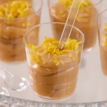 Fotografia em tons de branco com vários potinhos de plástico ao centro. Dentro de cada potinho existe uma receita de brigadeiro de colher de limão siciliano, finalizado com raspas de limão siciliano.