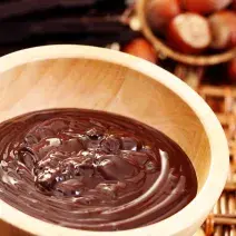 fotografia em tons de bege e marrom, tirada de um recipiente redondo bege com cobertura de chocolate dentro.