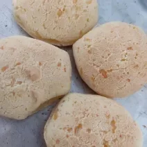 Fotografia de quatro pães de queijo sobre uma forma de alumínio.