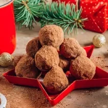 Fotografia mostra uma bandeja vermelha com trufas de chocolate perfeitas, cobertas com uma camada de chocolate em pó aveludado.