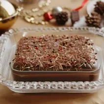 Foto da receita de doce abraço de natal, um pavê decorado com raspas de chocolate, lindíssimo e servido sobre uma mesa decorada com itens de natal