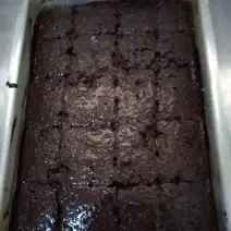 Fotografia de uma forma retangular de alumínio grande com um bolo e calda de chocolate com granulado.