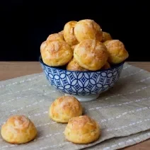 Fotografia em tons de preto com um prato azul estampado ao centro. Em cima do prato fundo, existe várias porções de doces feitos com massa Choux, uma massa aerada e leve.