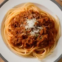 Fotografia de um espaguete com molho de carne e queijo ralado em cima, servido em um prato.