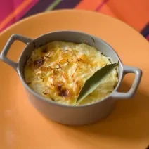 Fotografia de um recipiente pequeno que foi ao forno com uma receita de chuchu recheado com creme de milho e frango. A receita foi gratinada e tem uma folha de louro por cima.