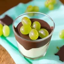 Foto da Receita de Bombom de Uva no Copo. Observa-se um copo de vidro com um creme baixo embaixo, por cima chocolate e decorado com uvas verdes. Foto gerada por IA.
