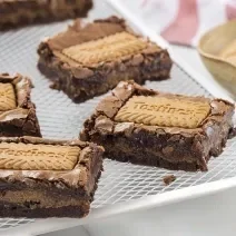 Foto da receita de Brownie de Tostines. Observa-se 5 fatias de brownie com o Biscoito TOSTINES Especiarias em cima e recheado de creme.