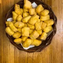 Fotografia em tons de marrom com uma cestinha de palha ao centro. Dentro da cestinha existe uma receita de pequenos cubinhos crocantes feito de tapioca e ovo na Air Fryer.