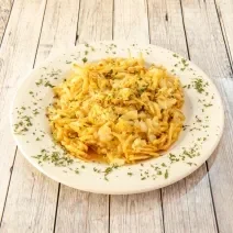 Fotografia de um bacalhau desfiado gratinado com batata palha, ovos batidos e requeijão. O bacalhau está em um prato branco fundo com salsinha picada e salpicada.