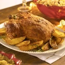 A fotografia apresenta um chester assado com crosta de creme de cebola, servido em uma travessa ao lado de batatas douradas.