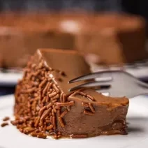 Foto da receita de Brigadeirão Sem Lactose. Observa-se uma fatia do Brigadeirão bem perto com chocolate granulado sendo cortada por um garfo.