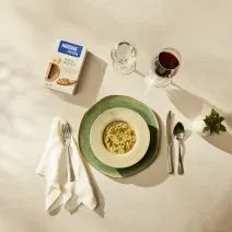 Fotografia em tons terrosos em um fundo bege com um prato verde, ao lado taça de vinho, embalagem de corte rustico.