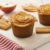 Fotografia em tons de marrom claro com uma tábua branca ao centro. Em cima da tábua existe duas tortinhas de maçã com alguns biscoitos TOSTINES ao lado.