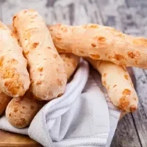 Fotografia em tons de cinza com uma toalha branca ao centro. Em cima da toalha existe vários biscoitinhos de polvilho dourados.