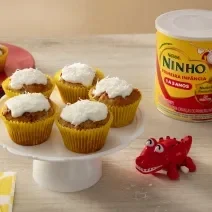 Fotografia em tons de amarelo e vermelho com 5 bolinhos ao centro. Por cima de cada bolinho existe um creme de leite de coco, coco ralado e NINHO Primeira Infância