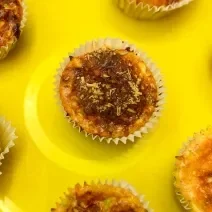 Fotografia em tons de amarelo com vários muffins de omelete ao centro. Em cima de cada muffin existe uma camada de queijo parmesão