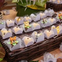 Fotografia de várias forminhas brancas com brigadeiro branco preparado com Leite MOÇA e gema, modelado em formato de animais. As forminhas estão sobre um apoio de madeira trançado.