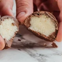 Foto da receita de Bombom de Prestígio. Observa-se uma foto bem perto do bombom cortado ao meio, expondo o recheio cremoso de coco.