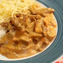 Foto tirada de cima de um prato azul com strogonoff de carne dentro, arroz e batata palha