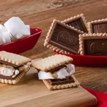 Fotografia em tons de vermelho com vários recipientes vermelhos ao centro. Dentro de um dos recipientes, existe dois biscoitos Choco Biscuit recheados com marsmallow. Ao lado existe marshmallows e biscoitos Choco Biscuit NESTLÉ