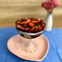 Fotografia em tons de rosa e azul com uma taça de vidro ao centro. Em cima da taça existe uma receita de açaí com frutas e ASCENDA