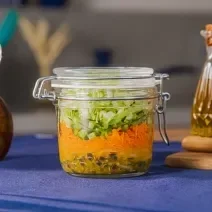 Fotografia em tons de azul com um pote de vidro ao centro. Dentro do pote existe uma receita de salada com molho de maracujá, cenoura e acelga