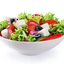 fotografia em tons de branco, verde, vermelho e preto tirada de um recipiente redondo branco com folhas de alface, fatias de tomates, queijo em cubo e fatias de azeitonas pretas.