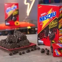 Foto da receita de Delícia Crocante de Chocolate. Observa-se a receita sobre um prato quadrado vermelho e, ao lado direito e atrás, 3 embalagens de NESCAU Cereal Extra Cacau.