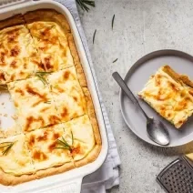 Fotografia mostra uma torta salgada coberta com uma superfície dourada e decorada com ervas frescas.