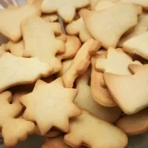 Fotografia em tons de caramelo com vários biscoitos amanteigados ao centro. Cada biscoitinho tem um formato diferente.