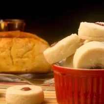 Fotografia de biscoitinhos amanteigados recheados com docinho de Leite MOÇA e NESQUIK de morango dentro de um recipiente de vidro branco e vermelho. Ao lado tem dois biscoitinhos jogados e no fundo tem um pão.