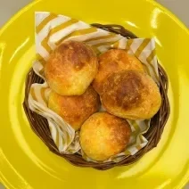 Fotografia em tons de amarelo com um prato amarelo ao centro. Dentro do prato existe uma cestinha com vários pãezinhos feito com queijo e Ninho Adulto