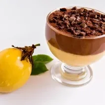 Receita de Mousse de Maracujá com Chocolate, fácil e delicioso, feito com Leite MOÇA, suco e maracujá concentrado, NESTLÉ Creme de Leite e Chocolate ao Leite NESTLÉ CLASSIC, servido em uma taça ao lado de uma maracujá