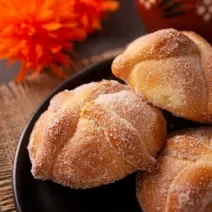 Fotografia de três unidades de pãezinhos recheados com doce de leite e passados na canela e no açúcar, os quais estão dentro de um recipiente preto fundo.