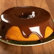 Foto da receita de Bolo de Cenoura. Observa-se o bolo em um prato de porcelana com calda de chocolate por cima escorregando.