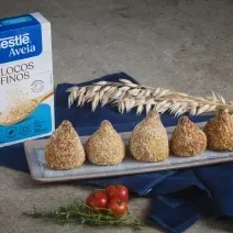 Foto da Receita de Coxinha da Batata Doce com Nestlé Aveia Flocos Finos, servidas em um prato cinza retangular, ao todo são 5, numa bancada de pedra com um tecido azul escuro, uma caixa de nestlé aveia flocos finos.