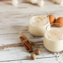 Receita de Gemada Clássica de Natal e Ano Novo, tradicional e deliciosa, feita com ovos, fava de baunilha, NESTLÉ Creme de Leite, Leite Líquido NINHO Forti+ Integral, conhaque e canela, servido em copinhos numa bancada de madeira