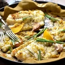 Fotografia de quatro filés de peixe assados com MAGGI MEU SEGREDO 7 Vegetais, ervas frescas e amêndoas. O assado está sobre papel manteiga e dentro de uma forma preta.